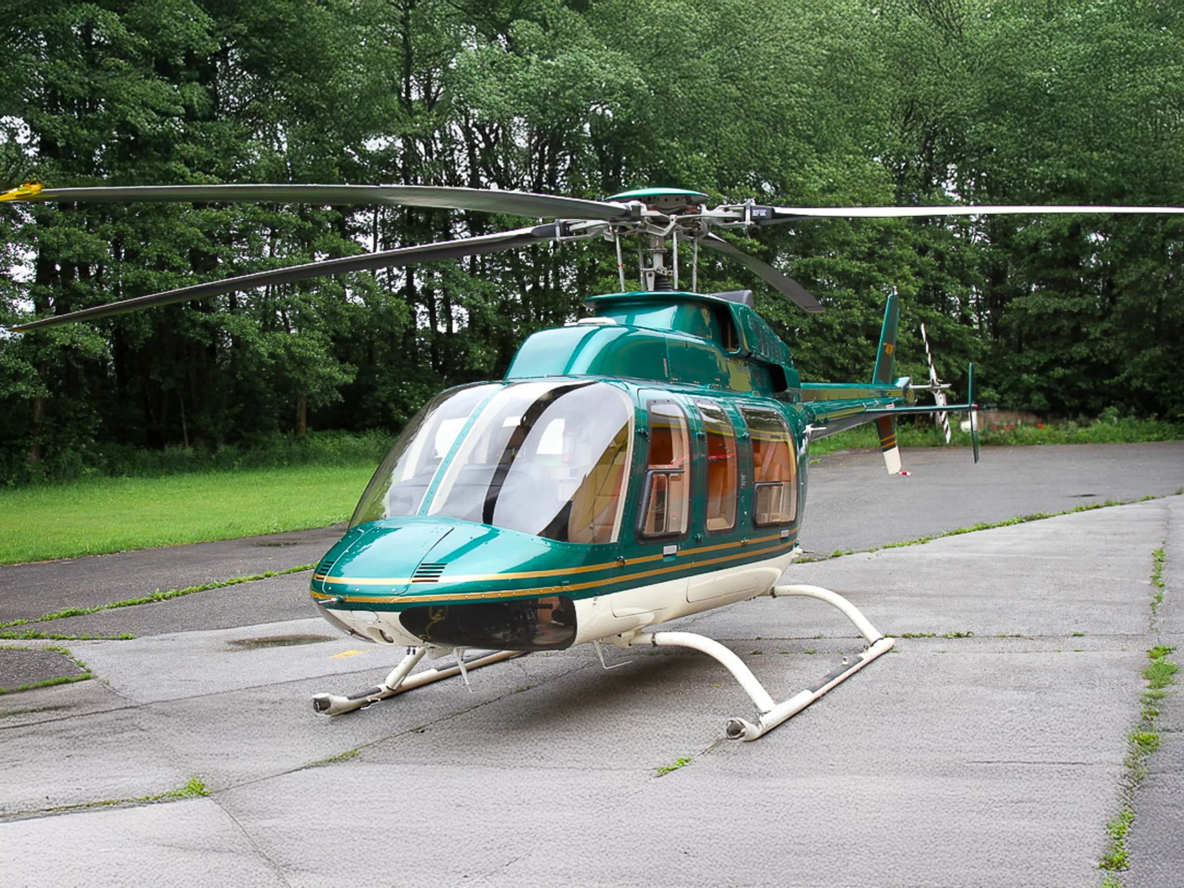 A Bell 407 helicopter with a green and white paint scheme is parked on the tarmac.