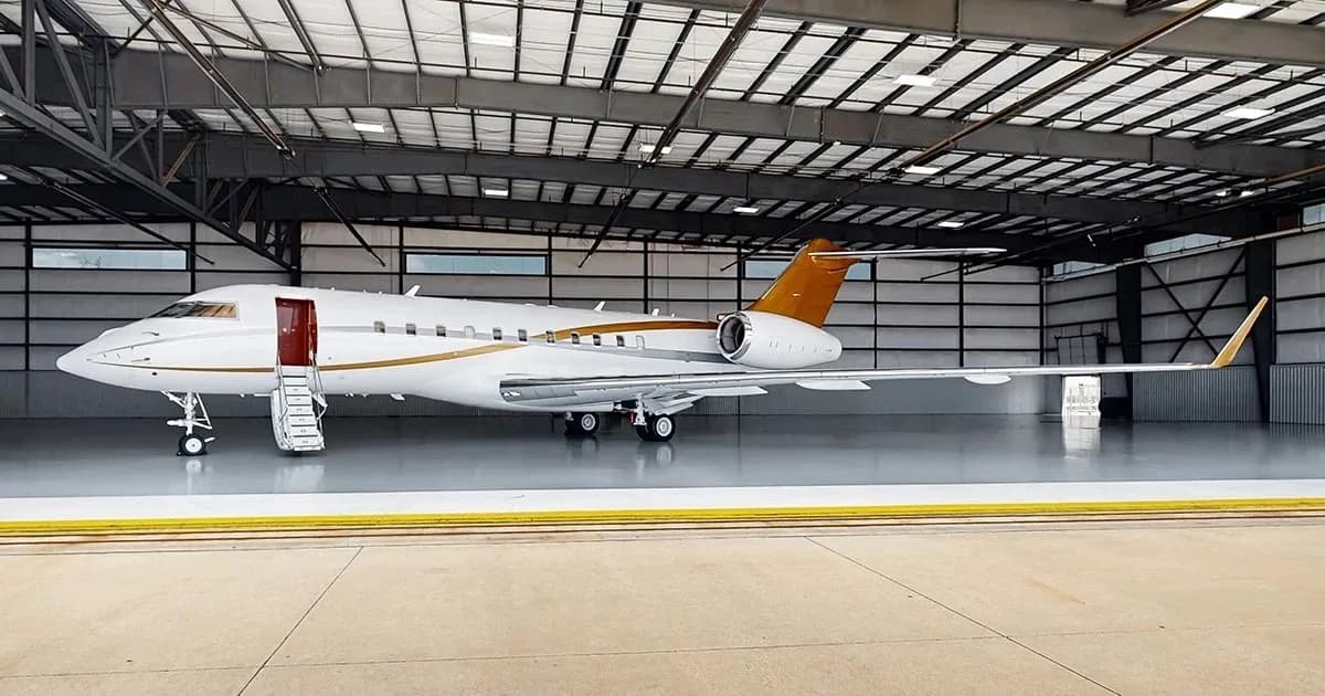 A white business jet with gold accents on the tail and fuselage is parked in a hangar with its main door open and stairs extended.