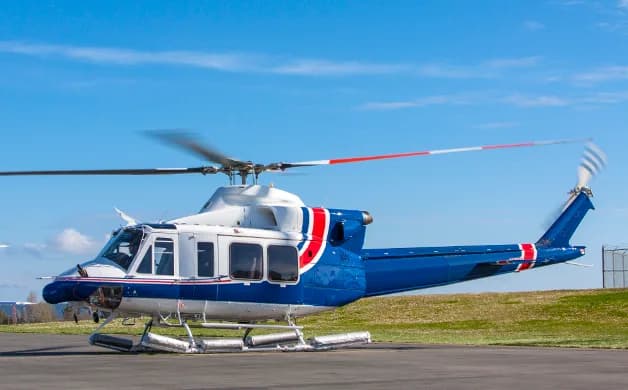 A blue and white Bell 212 helicopter with red stripes on an airfield under a clear blue sky.