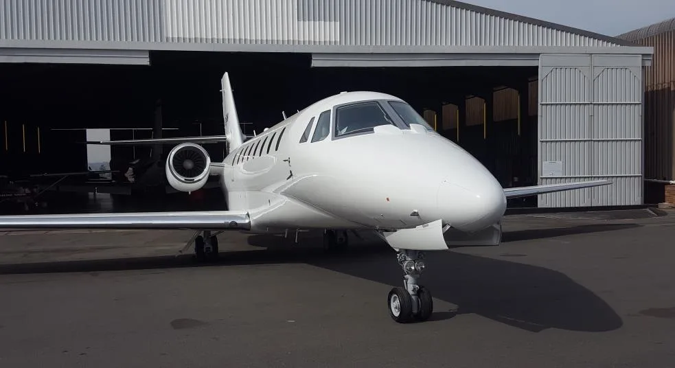 A white aircraft parked in front of an open hangar.