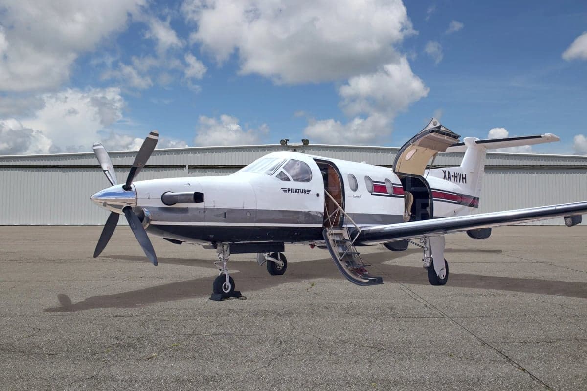 A Pilatus PC-12 aircraft is parked on the tarmac with its door and stairs open.