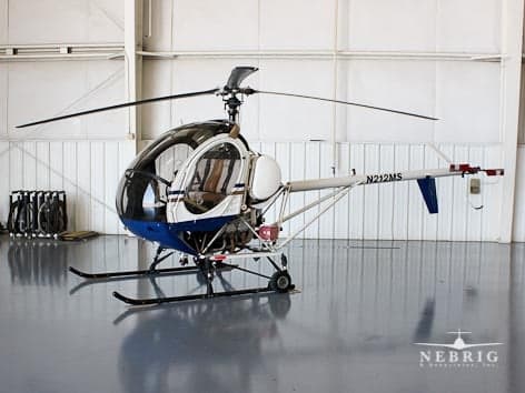 A white and blue Bell 47 helicopter, registration N212MS, parked inside a hangar.